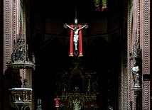 ▲	Krzyż z czerwoną stułą nad prezbiterium w ciemnej gliwickiej katedrze.