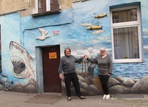 	Artysta razem z Ireną Korzeniewską przy morskim malowidle z jej obrazem i jej sylwetką.