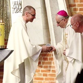 	Ksiądz kierownik wręcza biskupowi elbląskiemu pamiątkowy kubek pielgrzymkowy.