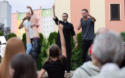 Ks. Dawid Fiołek na scenie z zespołem raperów.