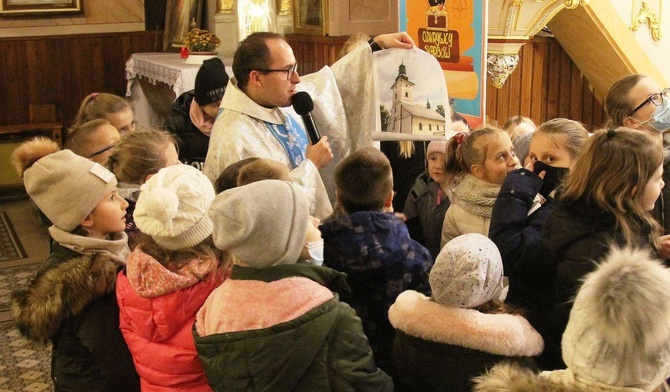 Ks. Marcin Samek prezentuje dzieciom zdjęcie kościoła św. Jakuba w Rzykach, znalezione w skrzyni tajemnic.