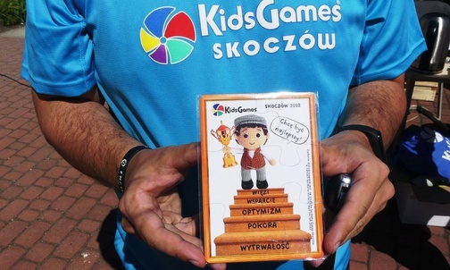 Ks. Przemek Guzior prezentuje magnes na lodówkę - pamiątkę 5. Igrzysk Kids Games w Skoczowie.