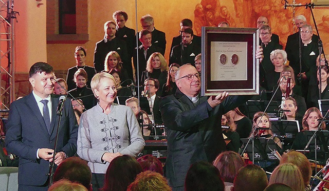 Ks. Fryderyk Tarabuła prezentuje medal Polonia Minor. Obok  –  Iwona Gibas i Rafał Kosowski.