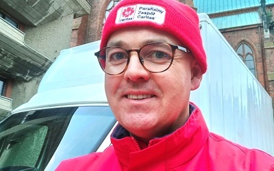Ks. Daniel Marcinkiewicz w czerwonym stroju z logotypem Caritas.