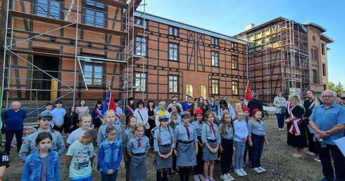 Najmłodsi uczestnicy pielgrzymki na tle dawnych budynków obozowych, które obecnie są poddane konserwacji.