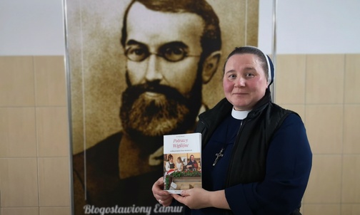 S. Monika Wrona z książką i portretem założyciela, który mógł jeść niektóre z wigilijnych potraw.