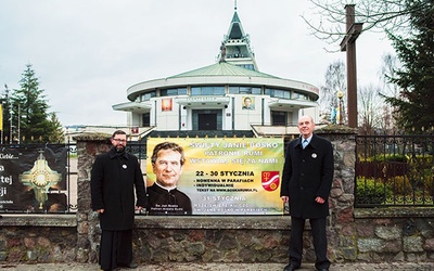 ▲	Ks. Rafał Burnicki SDB i Jan Klawiter z banerem zachęcającym do udziału w nowennie do świętego przed rumskim sanktuarium.