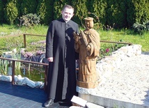 	Ks. proboszcz Rafał Wyleżoł przy rzeźbie patrona przy mostku jednej z alejek. 