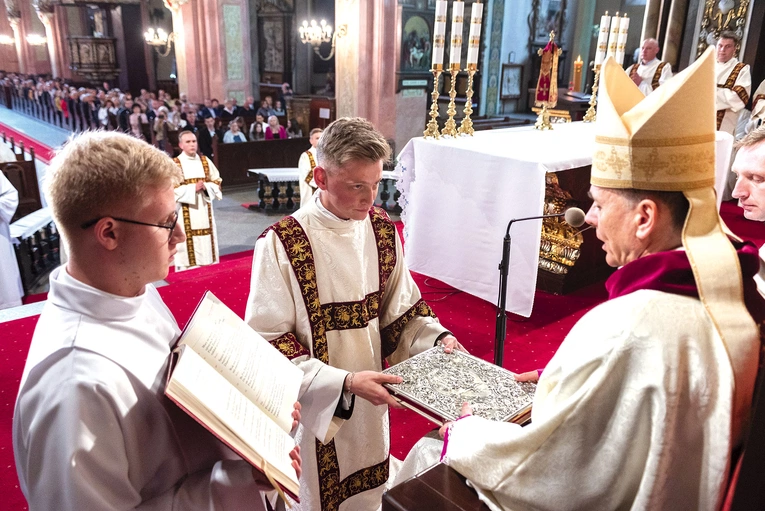 	Moment wręczenia księgi Ewangelii, podczas której biskup wypowiada słowa: „Przyjmij Chrystusową Ewangelię, której głosicielem się stałeś; wierz w to, co będziesz czytać, nauczaj tego, w co uwierzysz, i pełnij to, czego będziesz nauczać”.