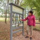 	Sołtys Barbara Mazurek przed tablicą ze zdjęciami „starych” Nieboczów – domami, gęsiami nad rzeką, łanami zbóż.