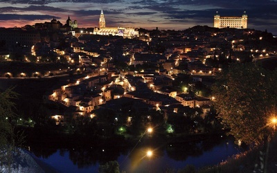 Panorama Toledo.  Ta dawna stolica  państwa Wizygotów  i późniejsza stolica Królestwa Hiszpanii została odzyskana  przez chrześcijan w 1085 roku. Dwa najbardziej oświetlone obiekty to gotycka katedra (w środku)  i alkazar (z prawej)  – dawna twierdza,  obecnie Muzeum Wojska.