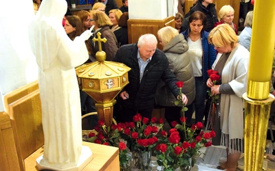Wierni składają róże przed figurą świętej.