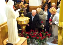 Wierni składają róże przed figurą świętej.