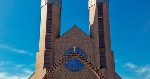 \Prowadząca do świątyni brama  ze słowami patrona: „Zachowaj łagodność wobec bliźniego i świętą pokorę przed Bogiem” oraz jego figurą.