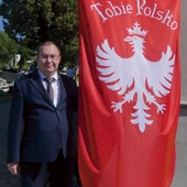 Archiwista żywieckiego cmentarza Przemienienia Pańskiego przy fladze powstańców śląskich. 