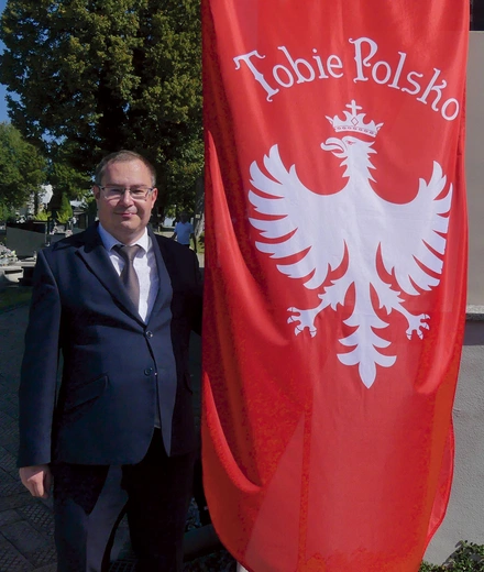 Archiwista żywieckiego cmentarza Przemienienia Pańskiego przy fladze powstańców śląskich. 