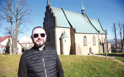 Ks. Rafał Słomba koło gotyckiego kościoła w Czchowie.