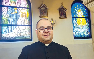 Ks. Piotr Siemek przy dwóch odnowionych oknach witrażowych.