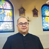 Ks. Piotr Siemek przy dwóch odnowionych oknach witrażowych.