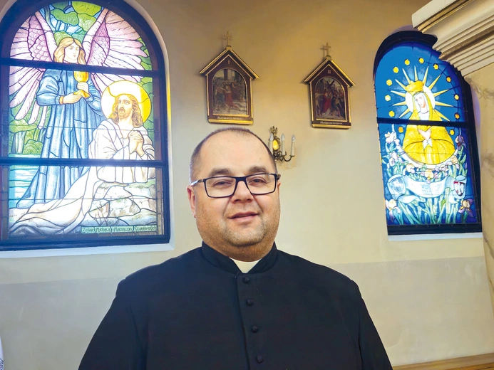 Ks. Piotr Siemek przy dwóch odnowionych oknach witrażowych.